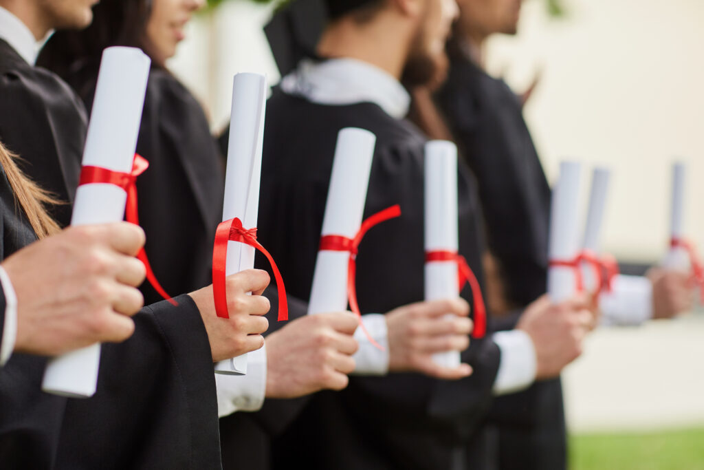 Scrolls of diplomas in the hands of a group of graduates. Graduation. University gesture and people concept.